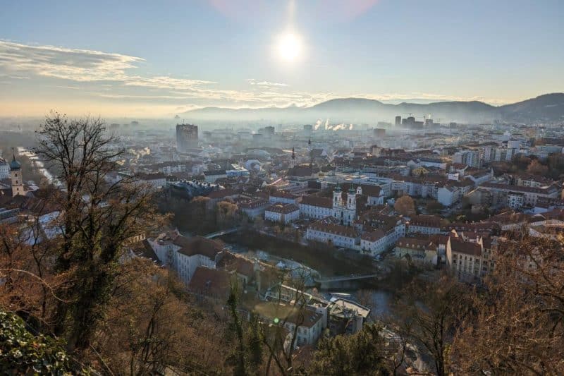 Panoramablick über die Grazer Altstadt mit Bergen und Sonne im Hintergrund