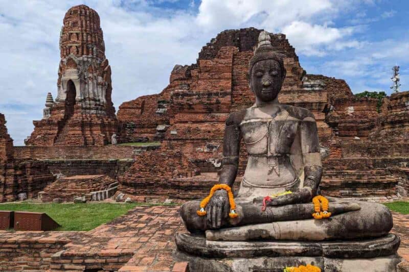 Verfallene Tempelruinen in Ayutthaya mit Buddha-Statue im Vordergurnd