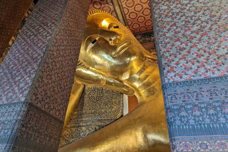 Kopf des riesigen Buddhas zwischen bunt verzierten Säulen im Wat Pho in Bangkok