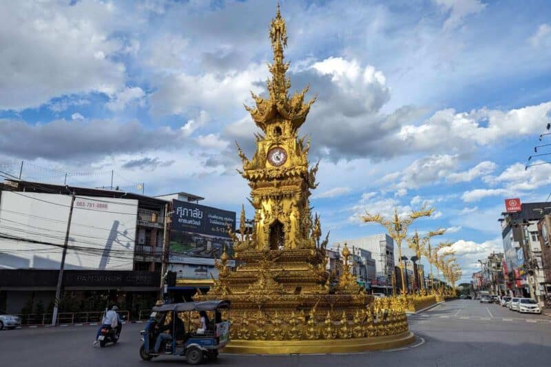 Der fein verzierte und vergoldete Uhrturm in einem Kreisverkehr mit Tuk Tuk in Chiang Rai