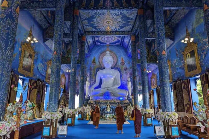 Ganz in Blau gehaltene Haupthalle des Wat Rong Sua Ten in Chiang Rai mit einer weißen Buddha-Statue am Kopfende