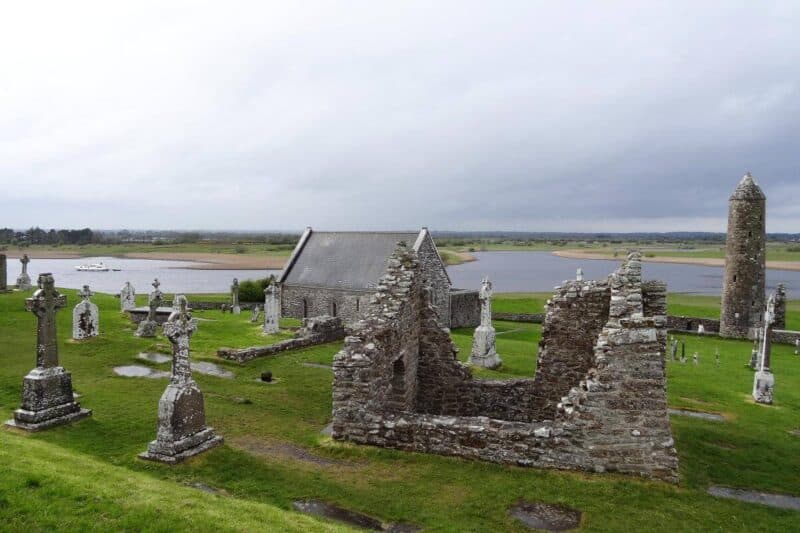 Kirchenruinen, Grabkreuze und ein Steinturm vor dem River Shannon in Clonmacnoise