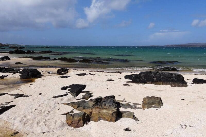 Heller Sandstrand mit schwarzen Felsen vor dem blaugrünen Meer in der Mannin Bay