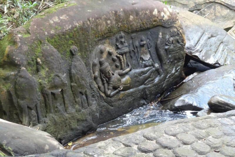 Ein in den Fels geschlagenes Relief einer liegenden Gottheit wird vom Wasser des Kbal Spean umspielt