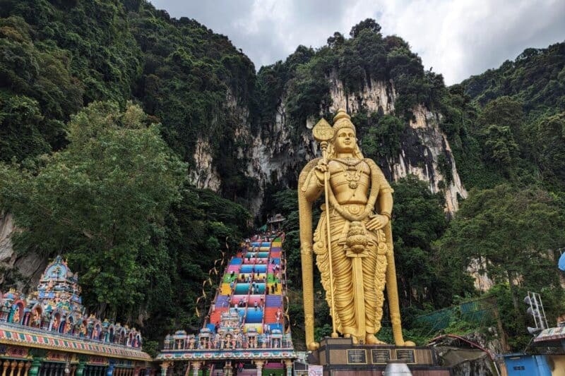 Die Felslandschaft der Batu Caves mit bunt bemalten Treppenstufen und der riesigen goldenen Statue des Gottes Murugan