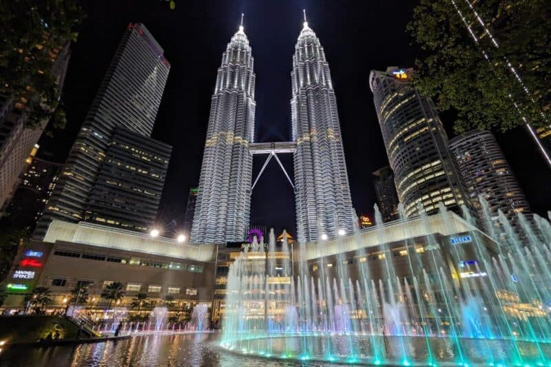 Die nächtlich beleuchteten Zwillingstürme der Petronas Twin Towers in Kuala Lumpur mit farbigen Wasserspielen im Vordergrund