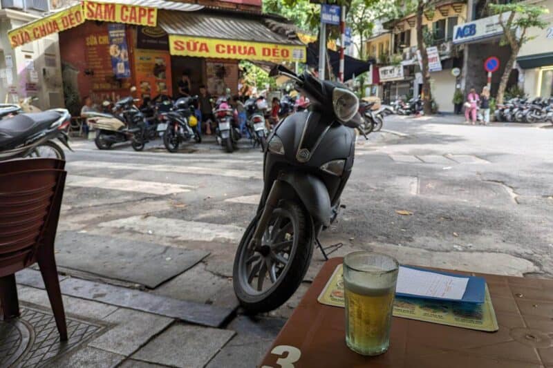 Ein Glas Bia Hoi auf einem Plastiktisch an einer Straße mit zahlreichen geparkten Motorrollern