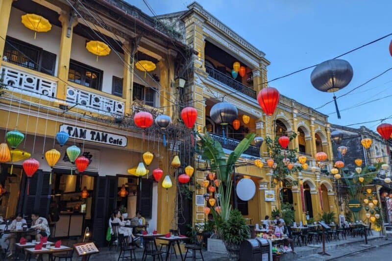 Bunte Lampions hängen in Hoi An von einem historischen Gebäude über die Straße