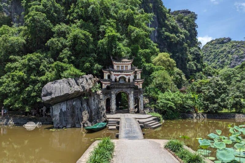 Eingangsportal der Bich-Dong-Pagode in Tam Coc mit einem Teich und einem Ruderboot vor steil aufragenden Karstfelsen