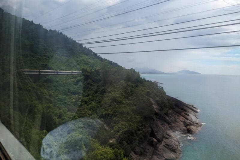 Ein Zug schlängelt sich über den Wolkenpassmit Blick auf Stromkabel und das Meer