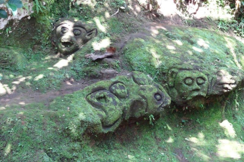 Steingravuren in den moosbewachsenen Felsen des Goa Gajah Sanctuary in Form von Tier- und Menschenköpfen