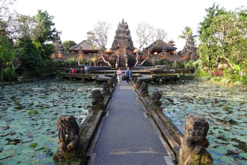 Eine Steinbrücke führt über einen mit Lotusblättern bewachsenen Teich zum Hauptturm des Ubud Water Palace