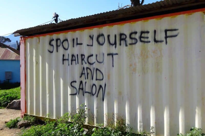 Schiffscontainer mit händisch aufgesprühtem Schriftzug "Spoil yourself Haircut and Salon" in Kayamandi